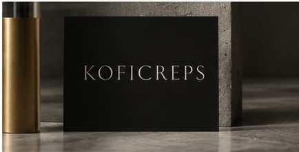 Caja negra mate con el logotipo KOFICREPS en marfil junto a un molinillo de latón.