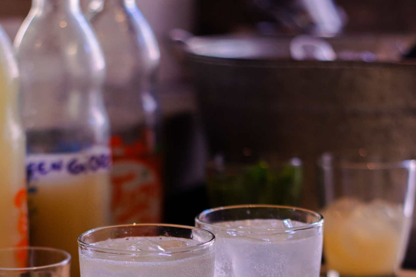 Dos vasos altos de limonada con hielo y hierbabuena, a contraluz sobre una bandeja de madera.