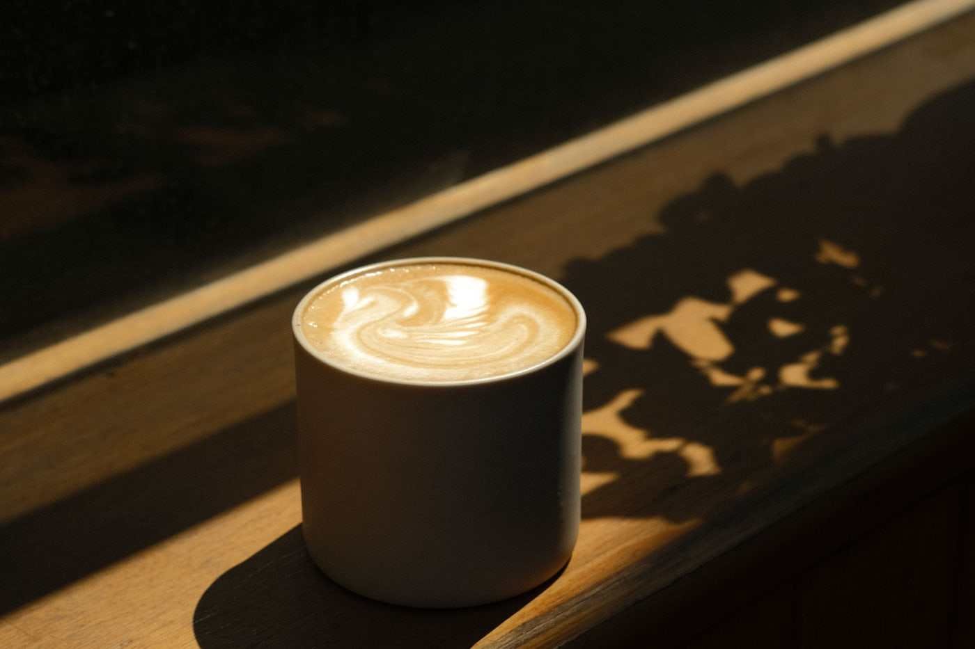 Taza de café oscura sobre una barra de madera, iluminada por una luz lateral dura.