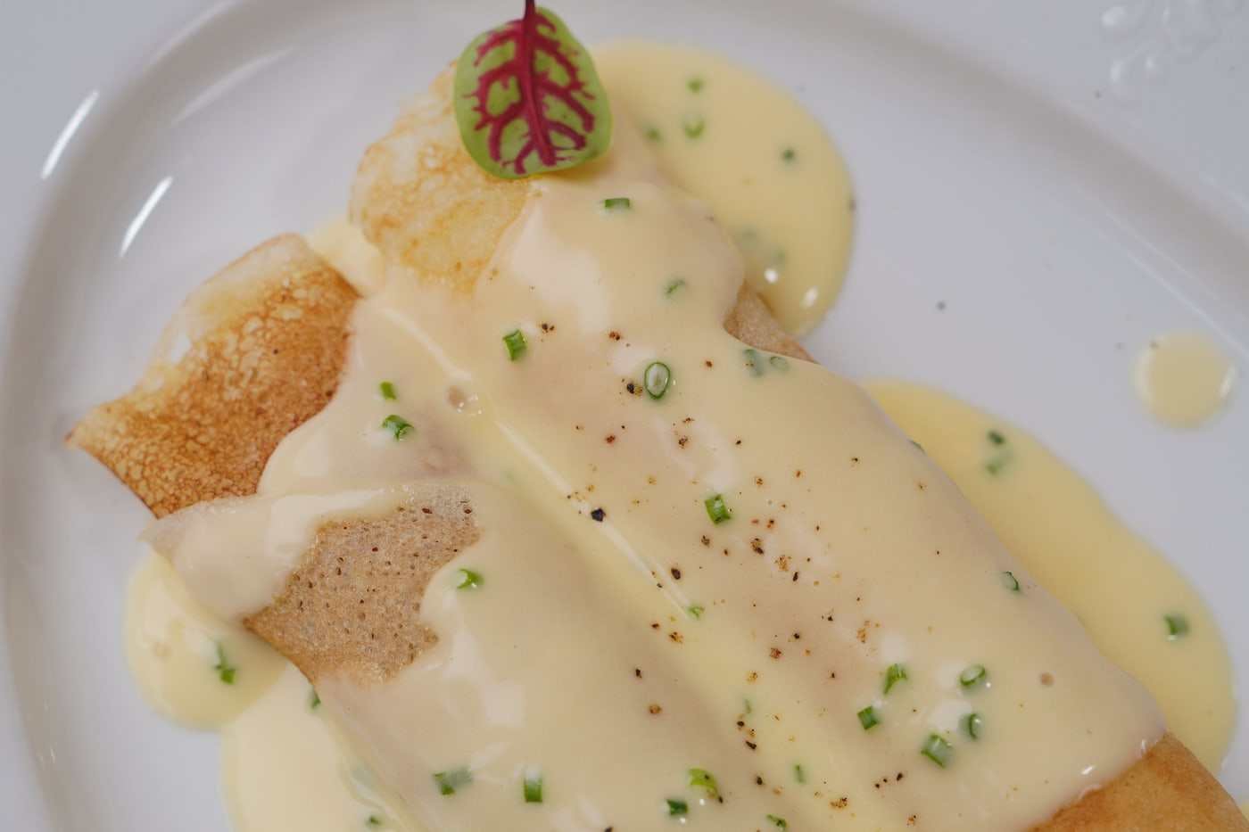 Crepe salada rellena y doblada sobre plato de cerámica mate, terminada con hierbas frescas.