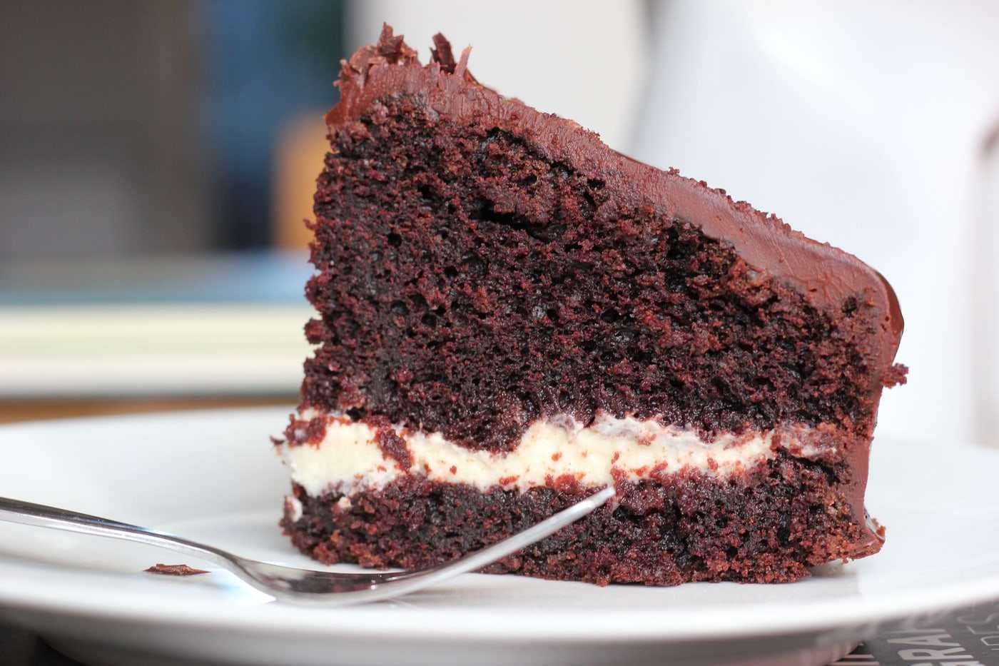 Porción de torta de chocolate de varias capas sobre plato claro, con fondo oscuro.