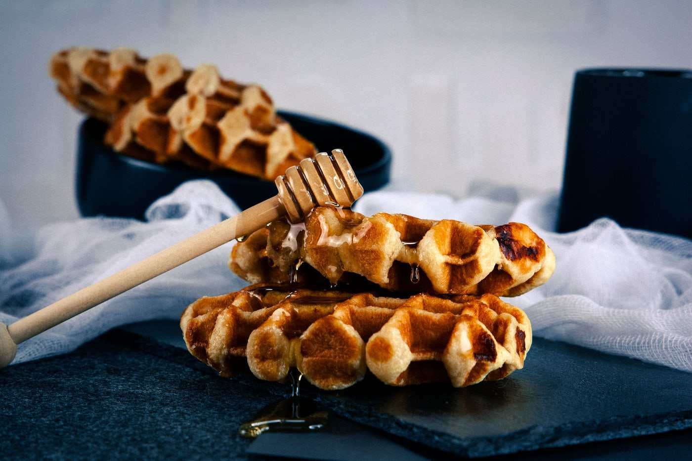Waffles recién hechos sobre pizarra oscura, con un hilo de miel cayendo por encima.